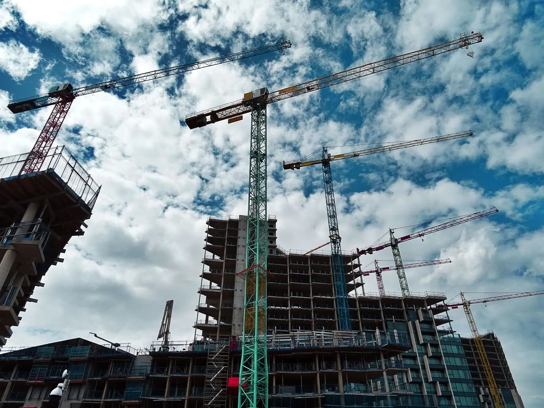 Cantiere urbano con numerose gru che incorniciano grattacieli in costruzione contro un cielo blu.