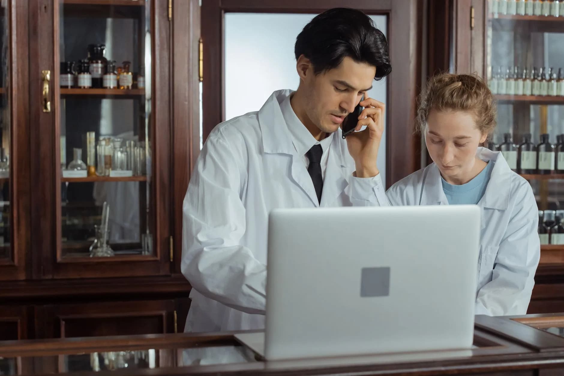 Due farmacisti lavorano insieme in una farmacia, utilizzando un laptop e un telefono per operazioni efficienti.